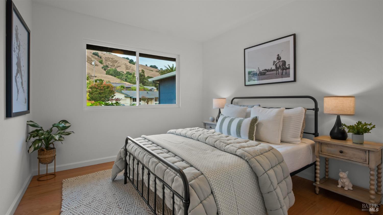 Staged bedroom with a black metal bed and a window overlooking dry hills.