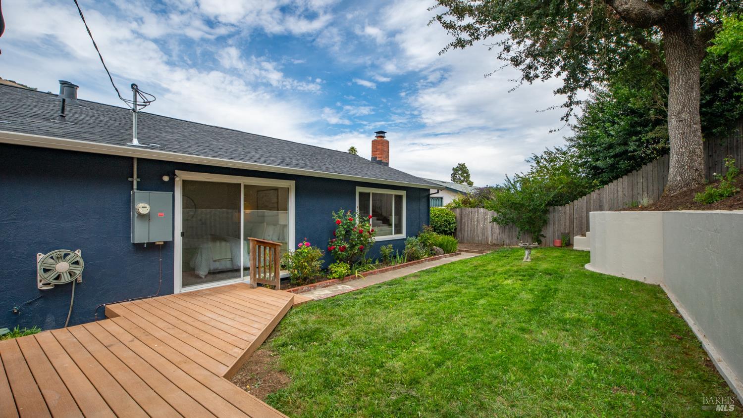 Rear yard with a wooden deck, lawn, fenced patio, and dark blue home exterior.