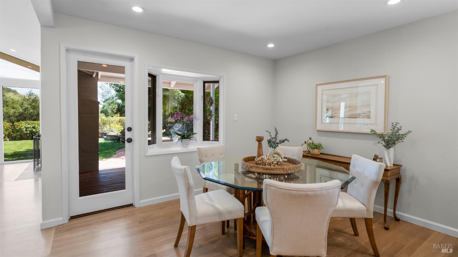 Dining room with a glass-top table and garden visible through the door and window.