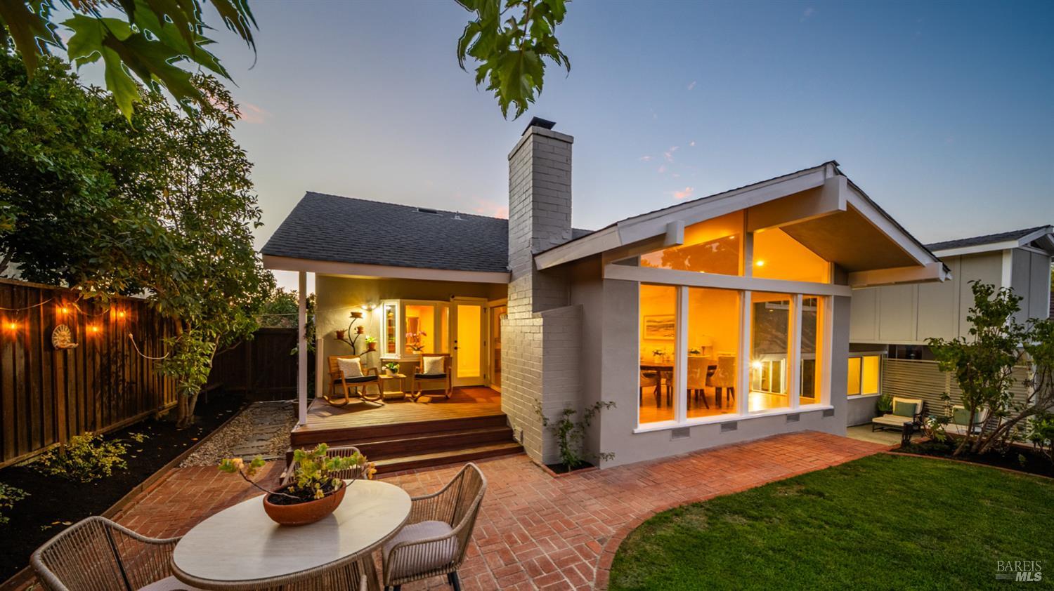 Modern home at dusk with glowing gabled windows, a brick patio, and a landscaped backyard.