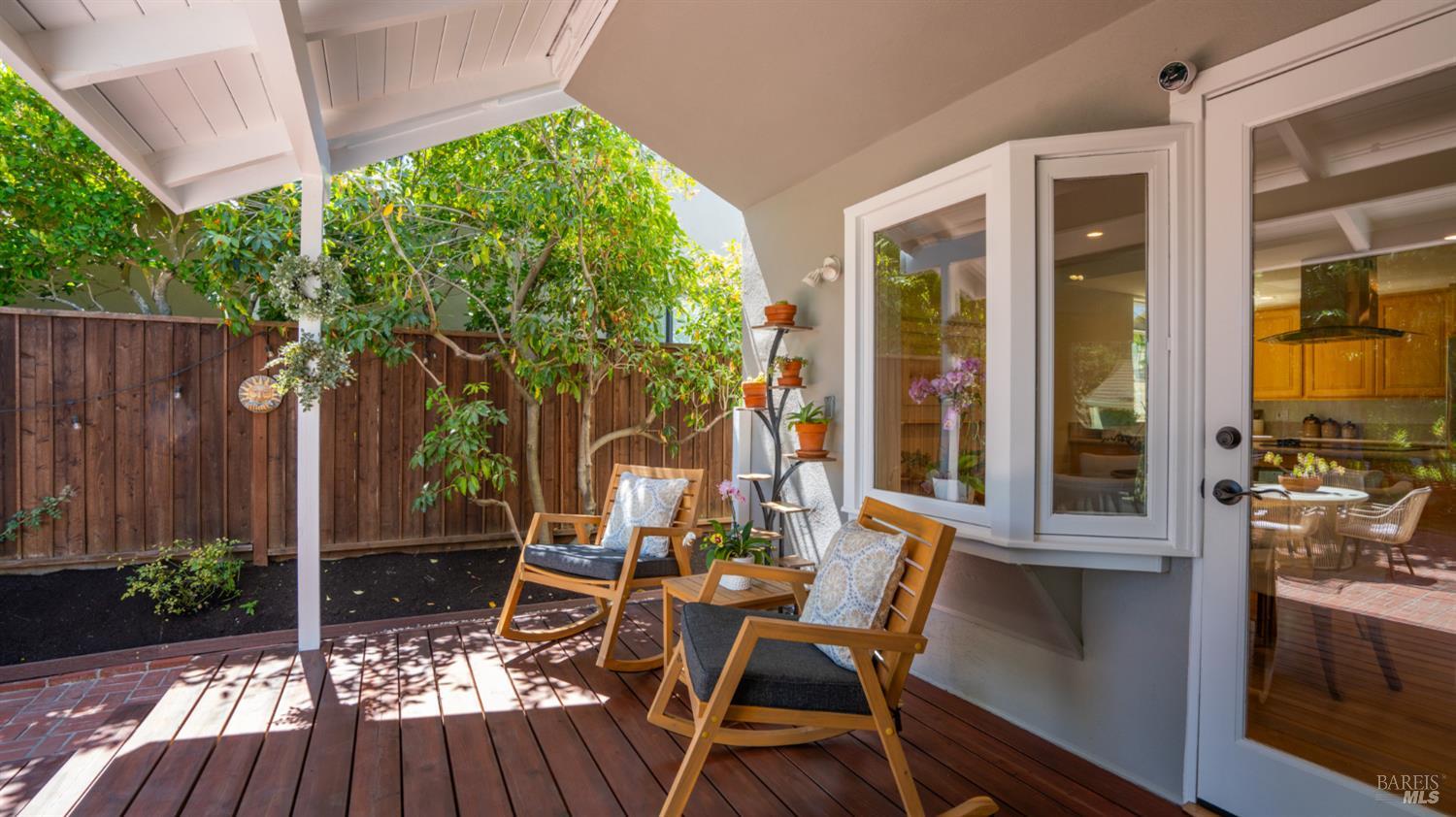Covered backyard deck with wooden rocking chairs, potted plants, and a leafy garden.