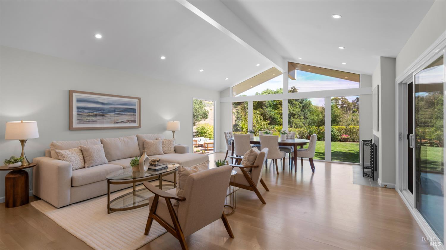 Open-plan living and dining room with tall garden-facing windows and pale wood floors.