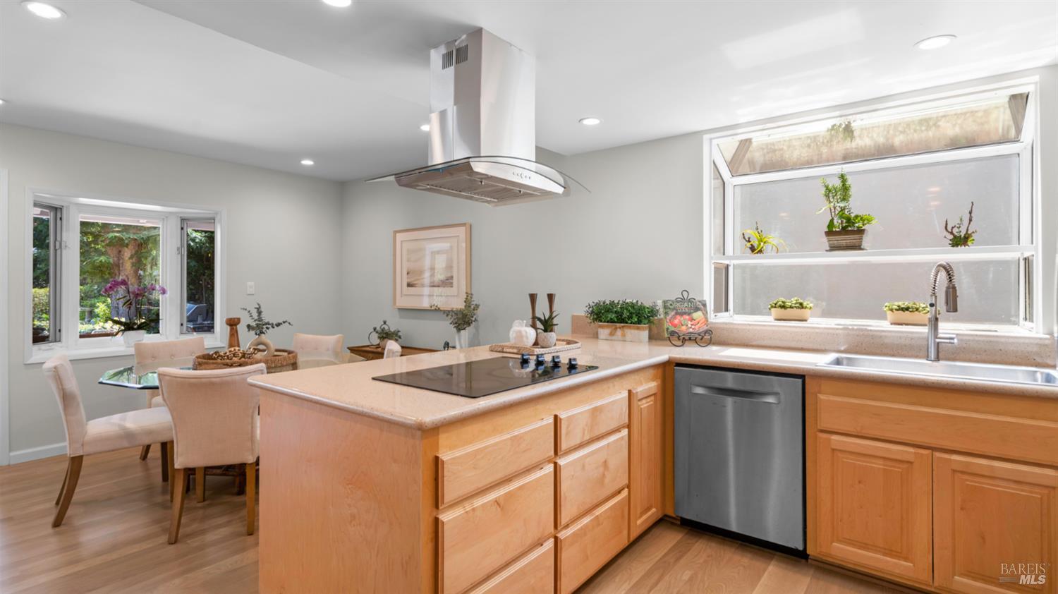Kitchen with a large cooktop island, light wood cabinetry, and windows overlooking the garden.