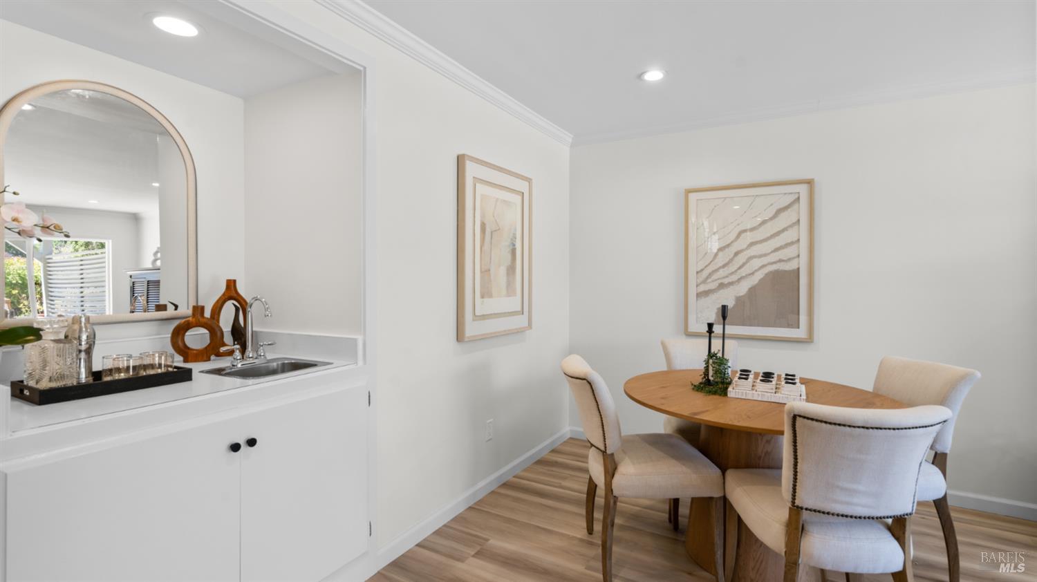 Dining room with a round wooden table, upholstered chairs, and a sink counter with an arched mirror.