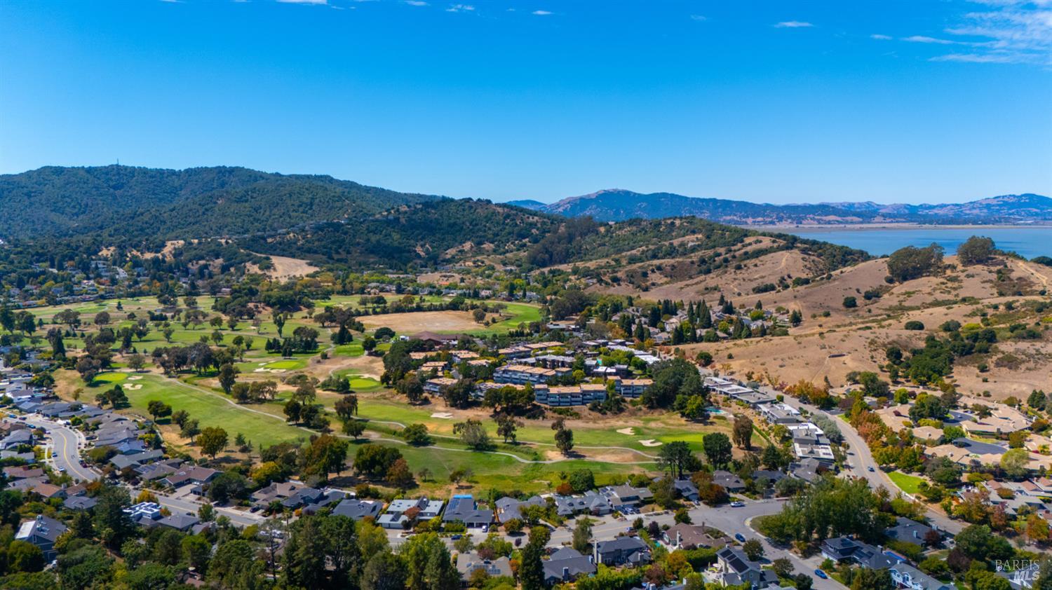 Aerial view of a San Rafael neighborhood, golf course, rolling hills, and water in the distance.
