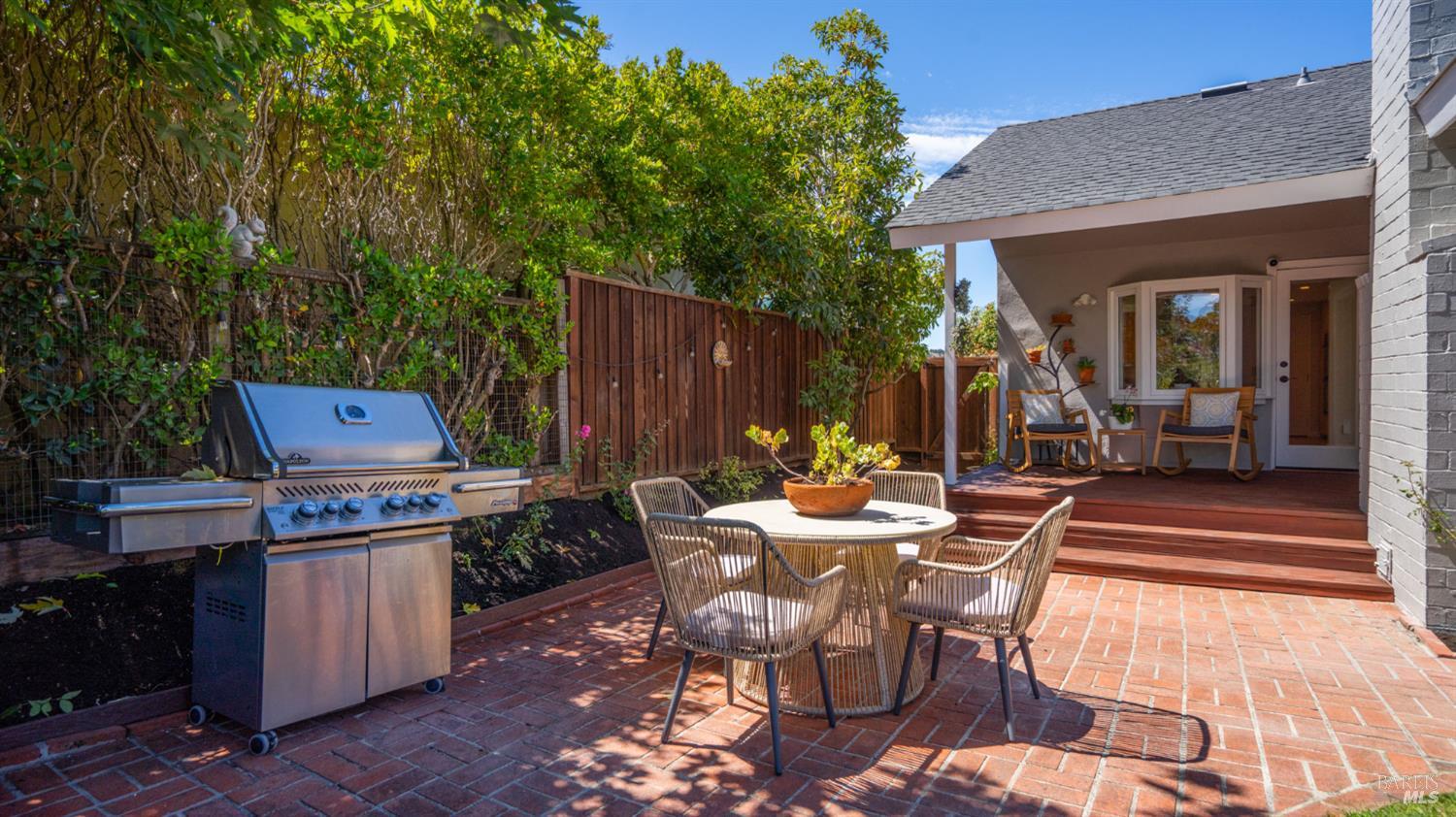 Backyard patio with brick paving, a dining set, stainless steel grill, and covered porch with rocking chairs.