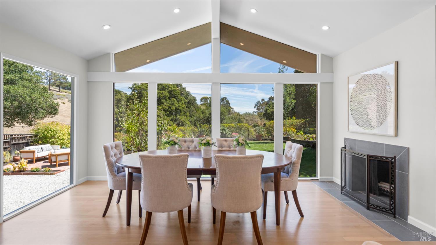 Dining room with a round table, vaulted windows overlooking the garden, and a tiled fireplace.