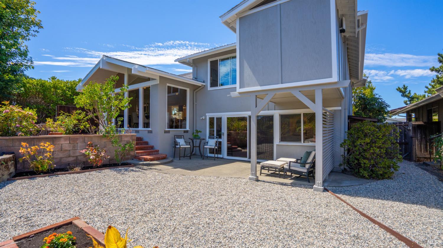 Gray two-story home with a covered patio, sliding doors, outdoor seating, and a gravel courtyard.