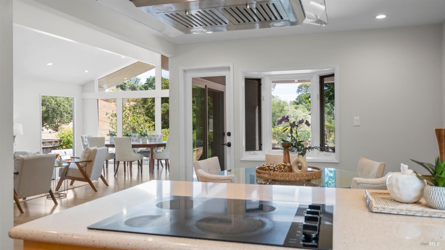 Bright kitchen with a large cooktop island, open dining area, and expansive garden-facing windows.