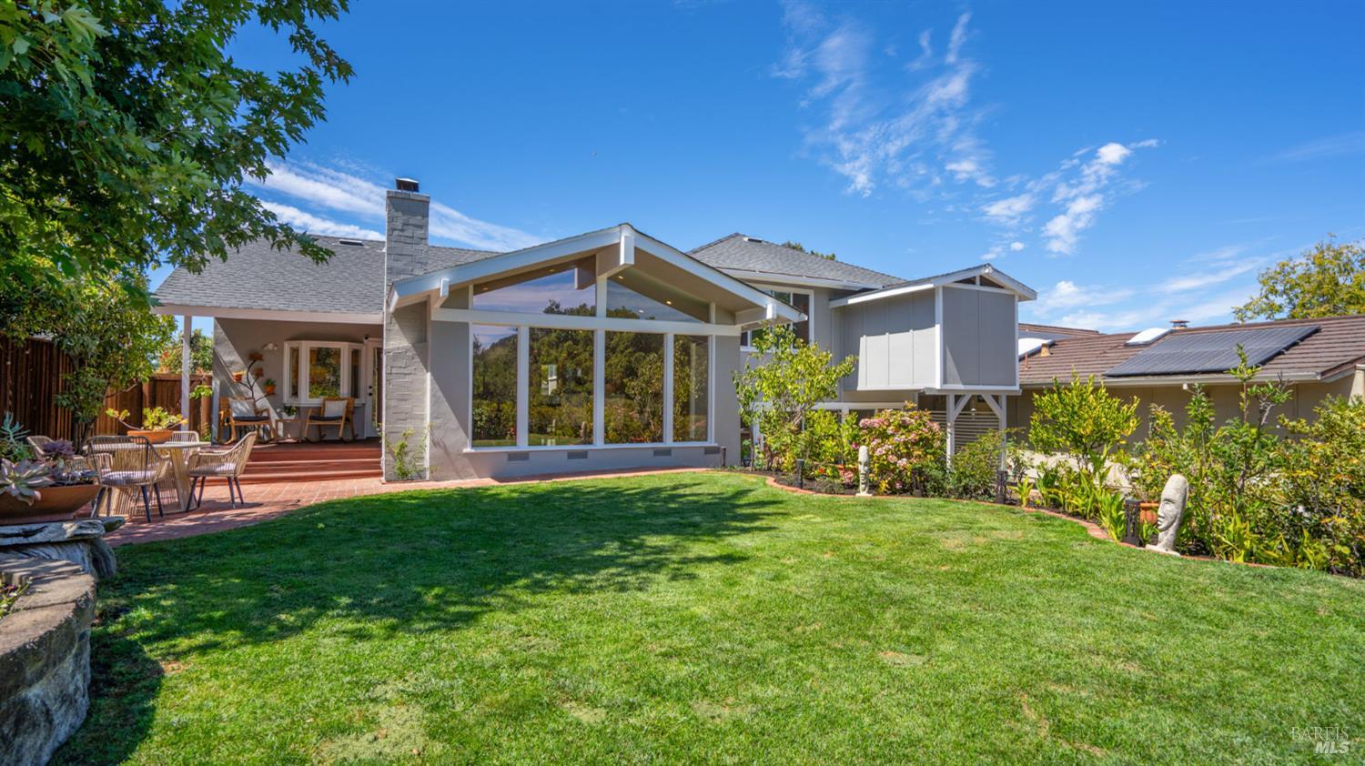 Rear exterior of a single-story home with a broad lawn, glass gable window, and brick patio.