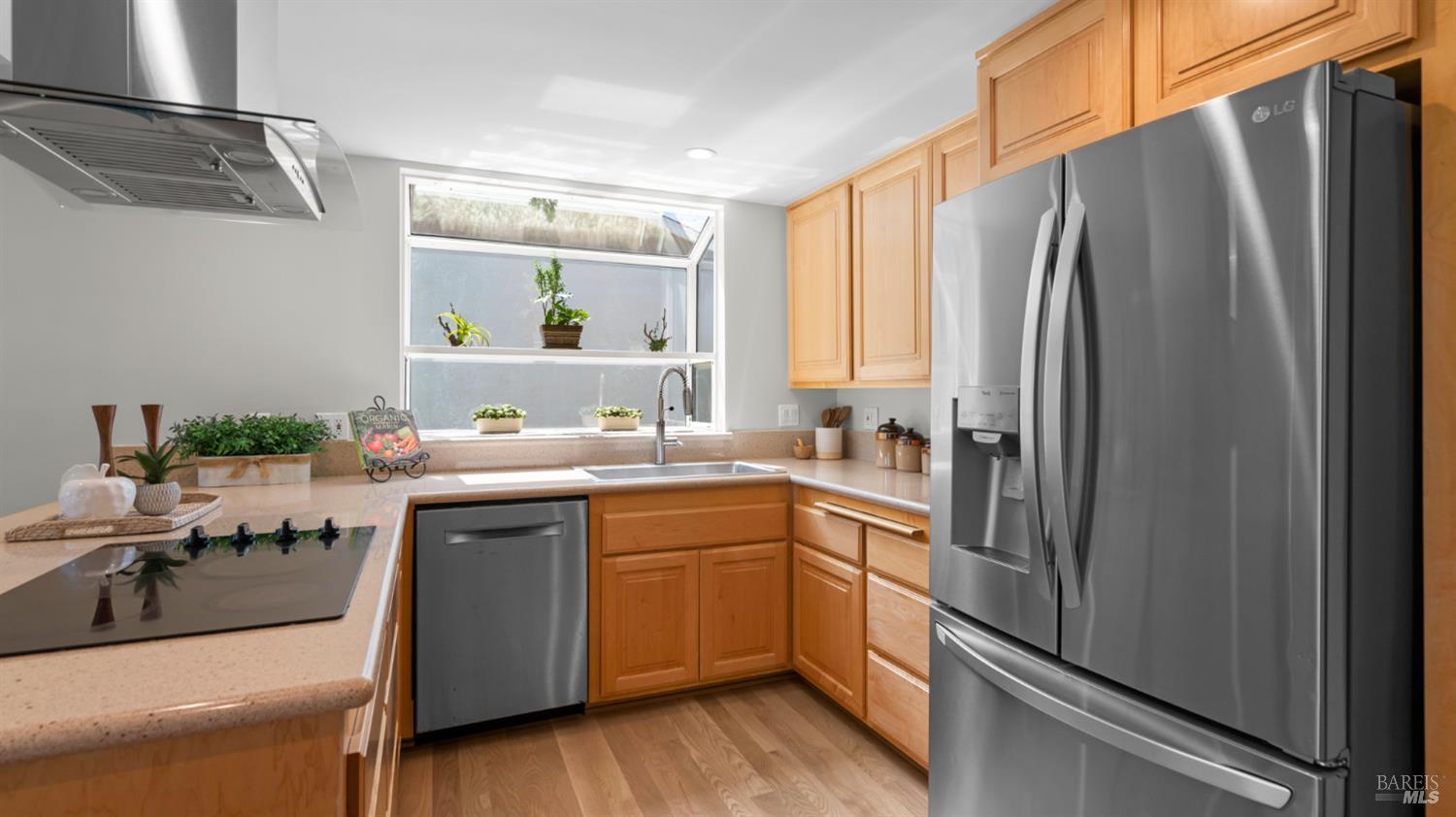 Kitchen with honey-toned cabinets, stainless steel appliances, and a sink beneath a wide window.