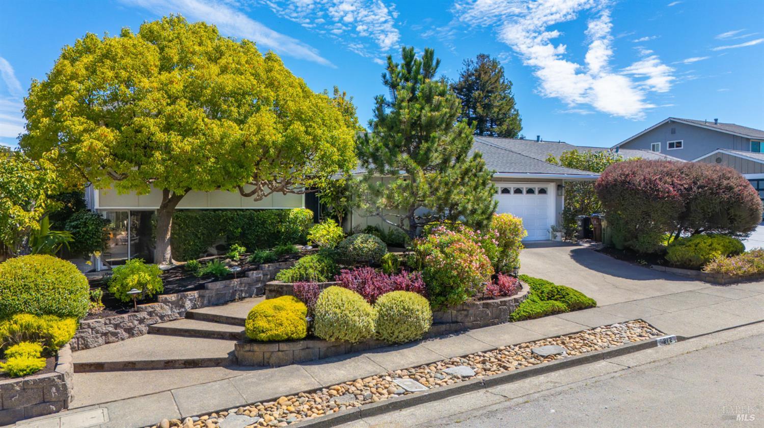 Single-story home with a white garage door, broad driveway, and colorful landscaped front garden.