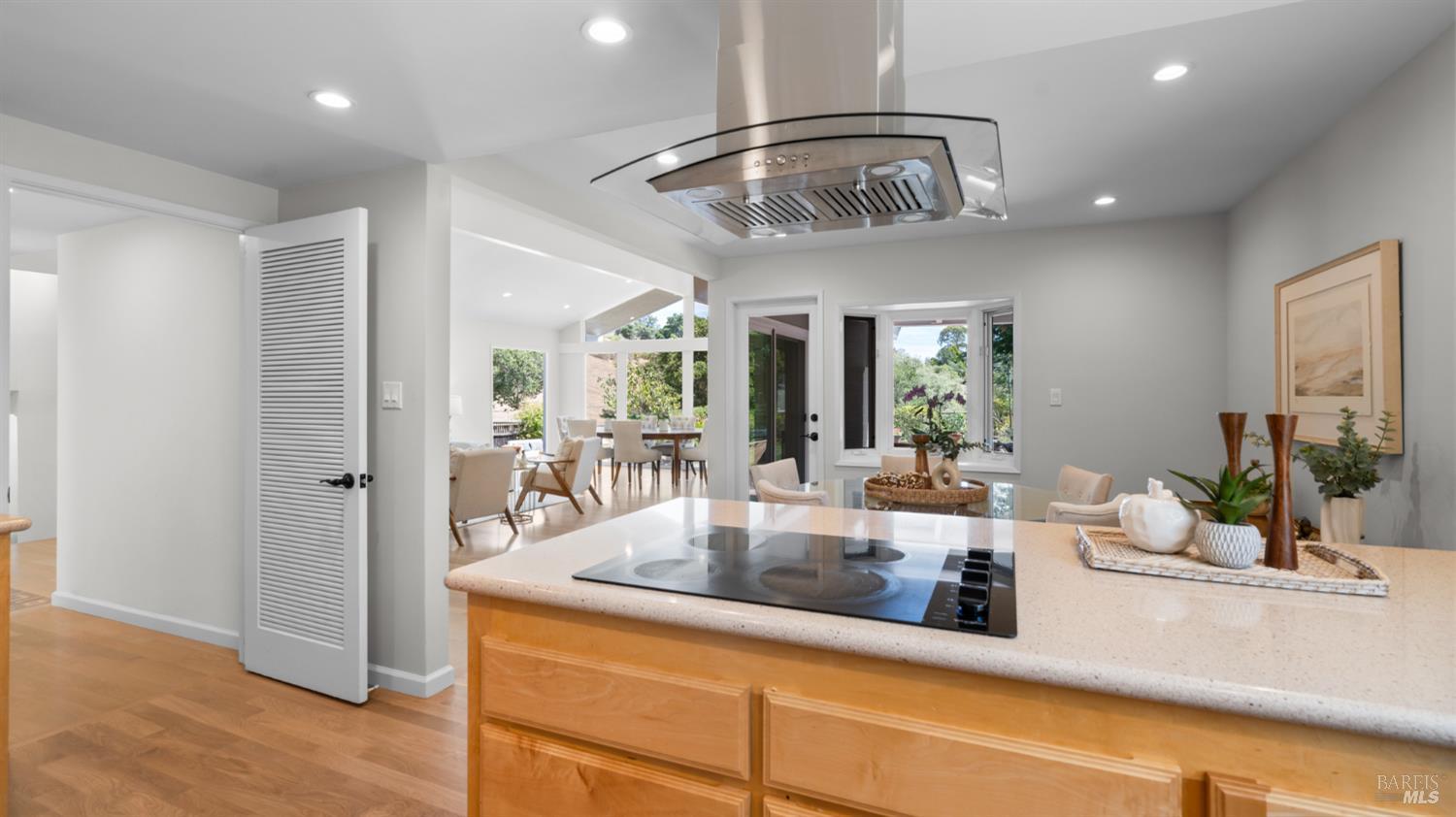 Kitchen with a wood island and cooktop, opening to a bright dining area with garden views.