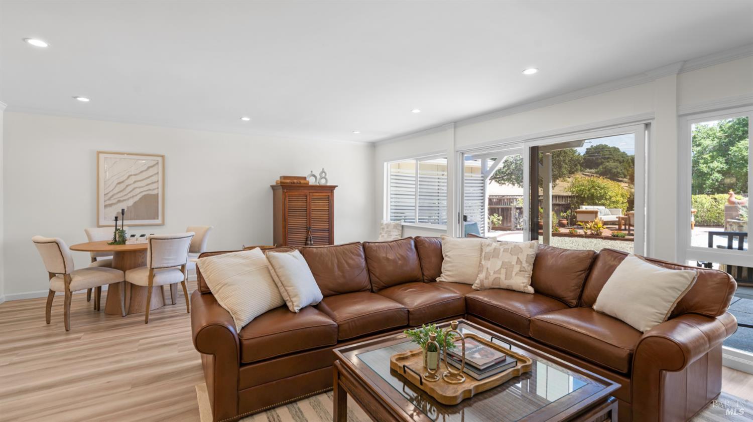 Living and dining room with a brown leather sectional and sliding doors opening to a landscaped patio.