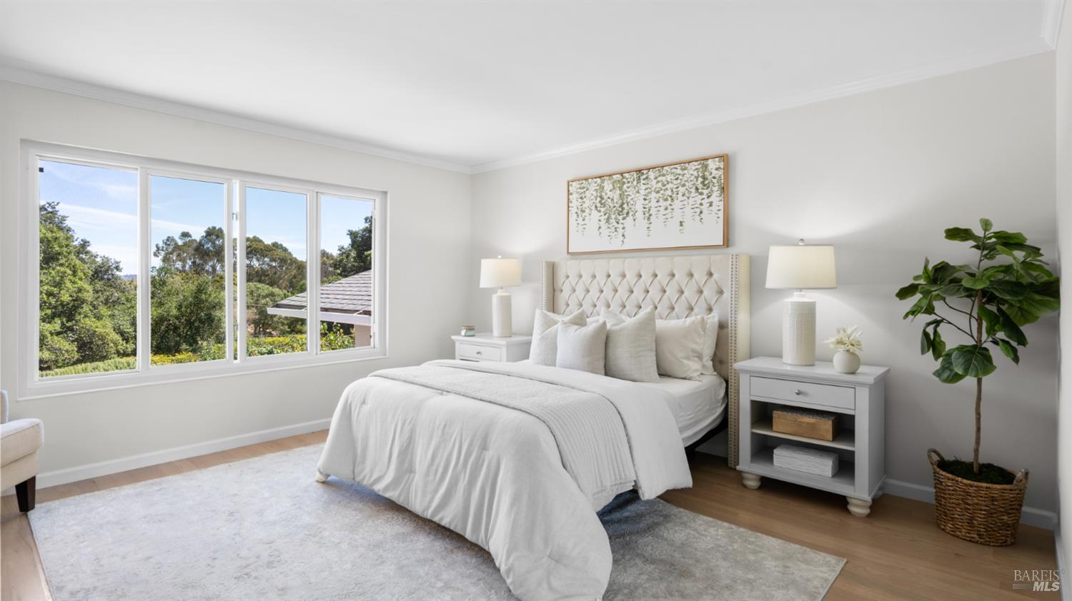 Staged bedroom with a white bed, large window overlooking trees, and potted plant.