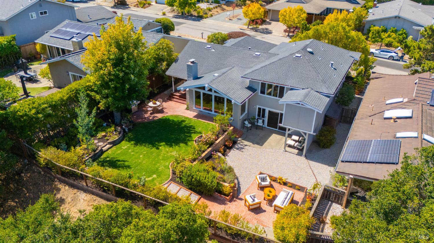 Aerial view of a two-story home with a landscaped lawn, brick patios, and rooftop solar panels.