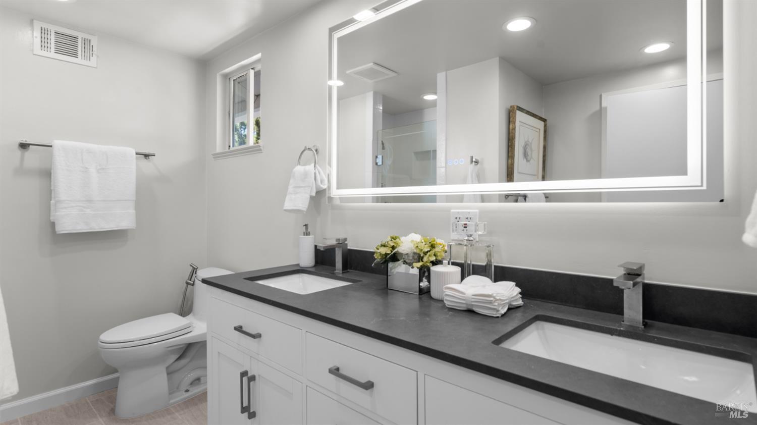 Modern bathroom with a double-sink vanity, dark countertop, and large illuminated mirror.