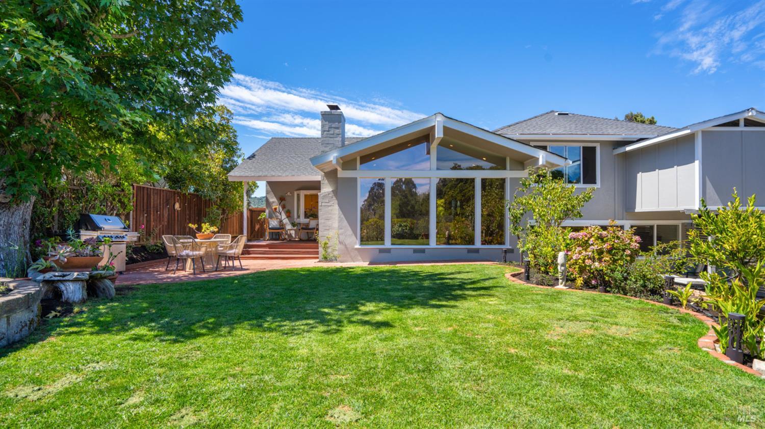 Home’s rear exterior with a glass-fronted gable, broad lawn, and furnished brick patio.
