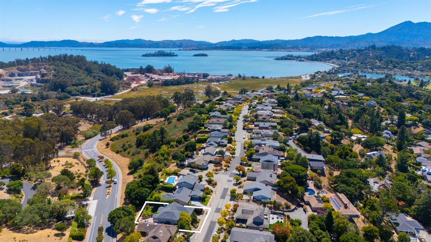 Aerial view of an outlined home among trees, with the bay and distant mountains beyond.