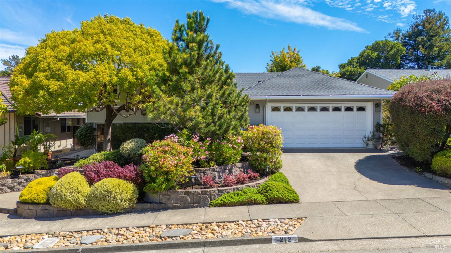 Single-story home with a white double garage, broad driveway, and colorful landscaped front garden.