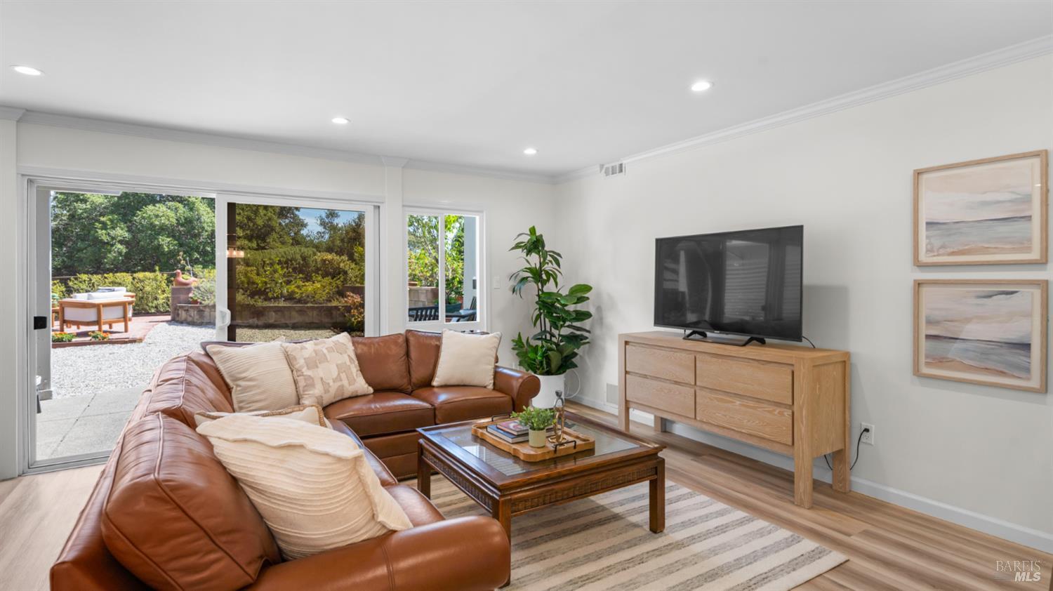 Living room with a brown leather sectional and sliding glass doors opening to a garden patio.