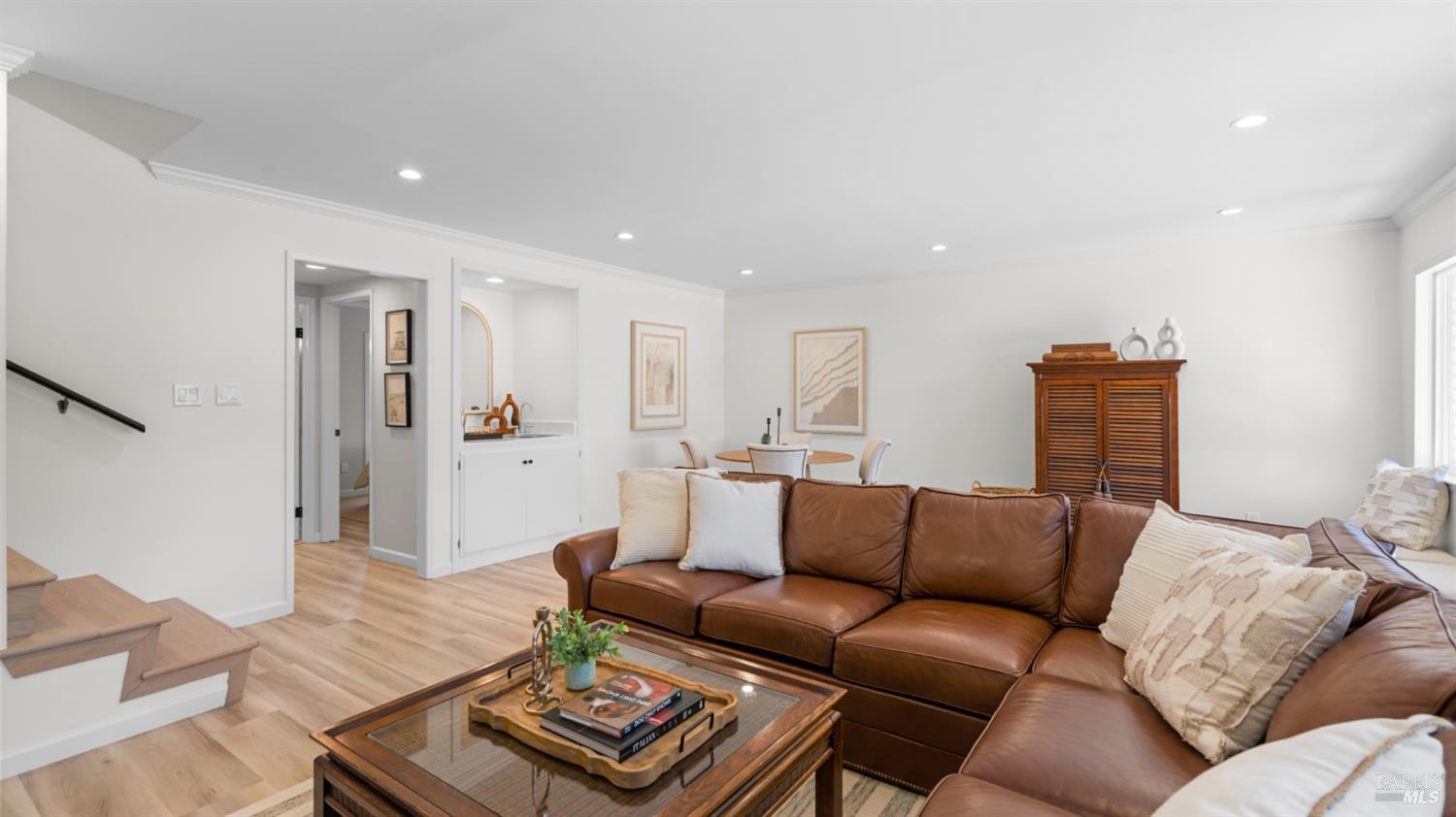 Furnished living room with a brown leather sectional, glass-top coffee table, and light wood floors.
