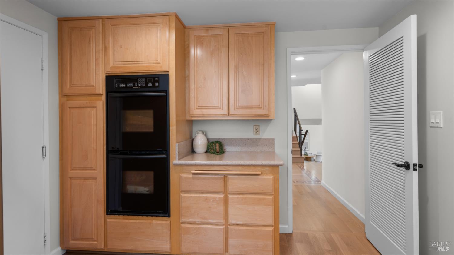 Built-in kitchen cabinetry with a black double oven beside an open doorway to the hall.