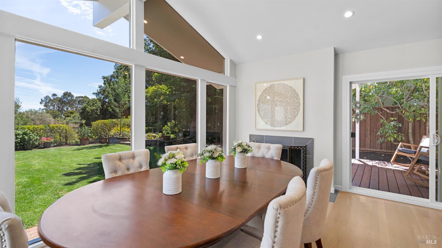 Dining room with an oval wood table, tall garden-facing windows, and a fireplace.