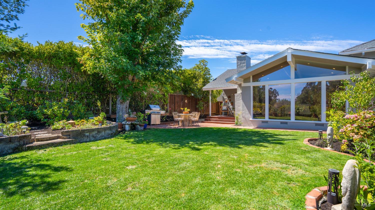 Backyard with a broad lawn, mature trees, and a covered patio with outdoor dining furniture.