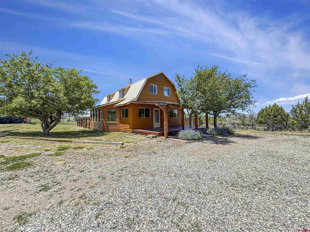 Brown two-story house with a light metal roof and covered porch in a gravel yard.