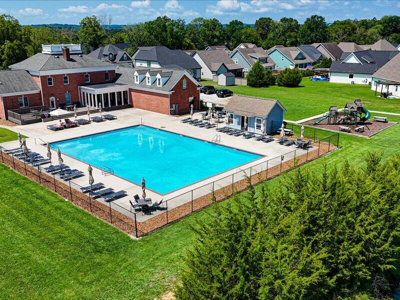 Outdoor community pool with lounge chairs, clubhouse, and playground among neighborhood homes.