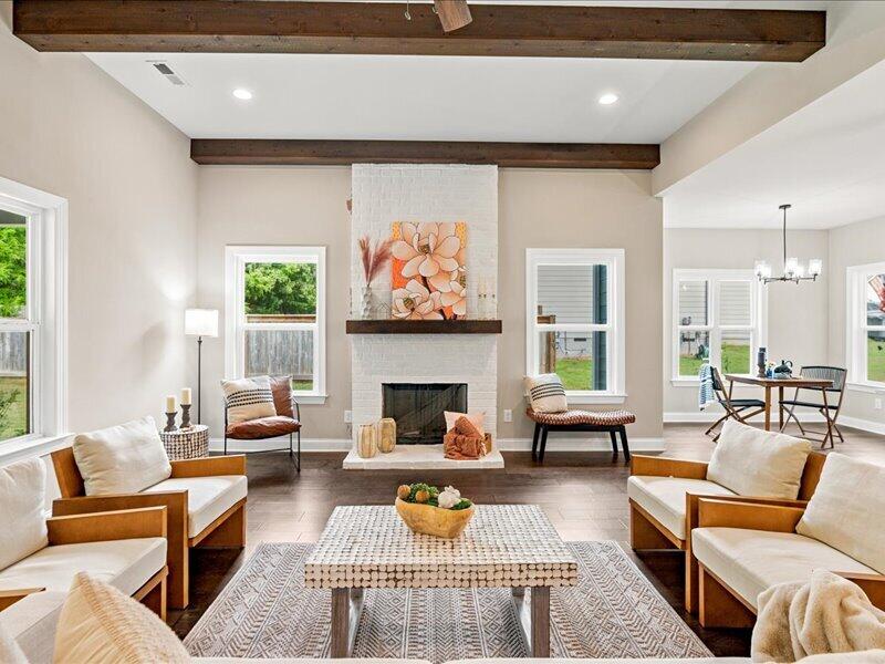 Living room with a white brick fireplace, exposed ceiling beams, and dining area beyond.