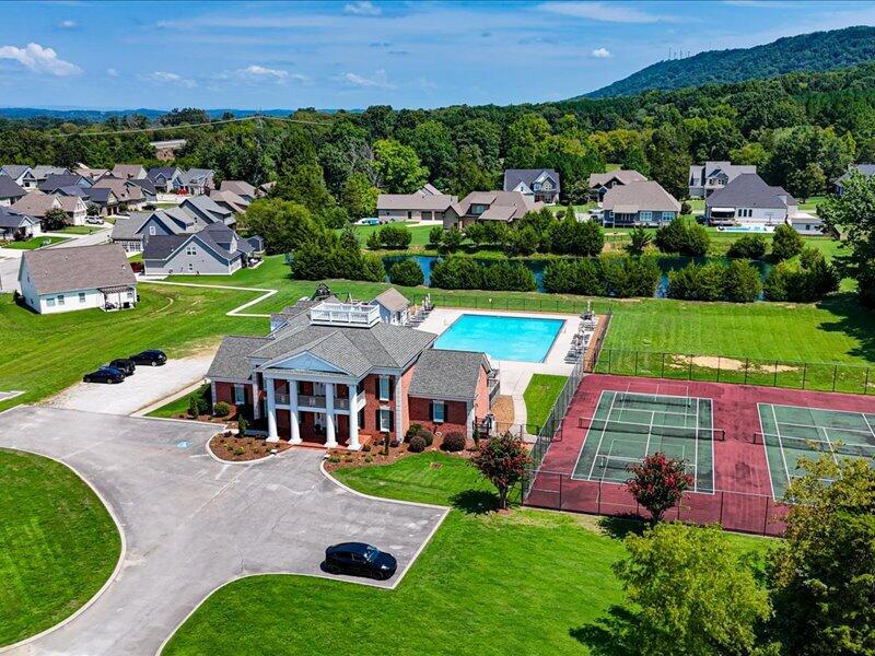 Residential community clubhouse with a swimming pool, tennis courts, and wooded mountain backdrop.