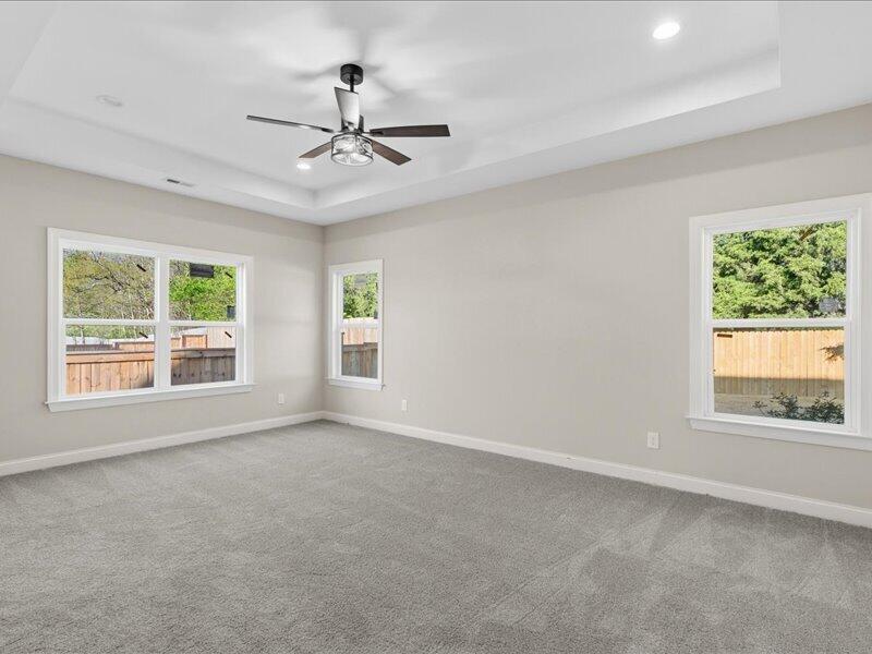 Empty carpeted room with three windows, a ceiling fan, and a recessed tray ceiling.