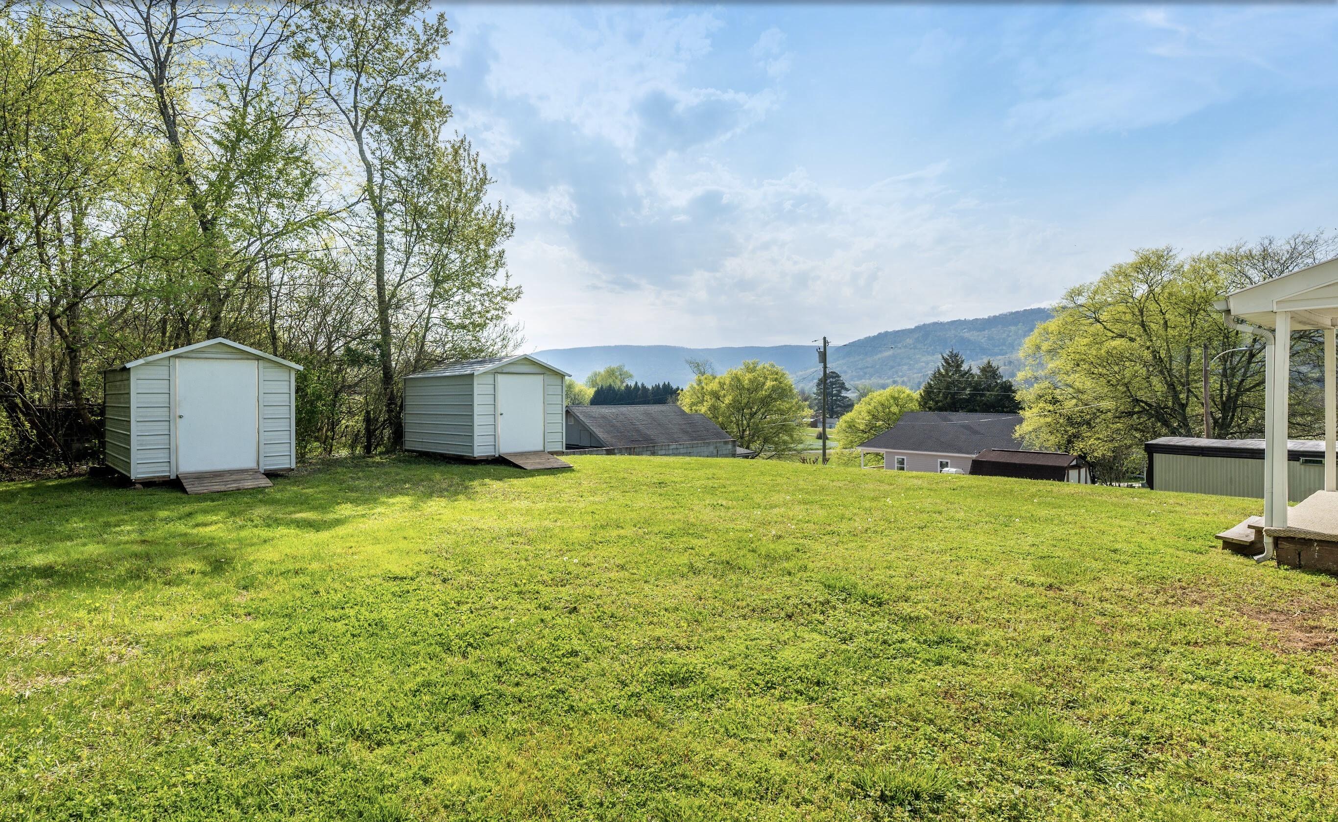 Grassy backyard with two storage sheds and a wooded mountain ridge beyond.