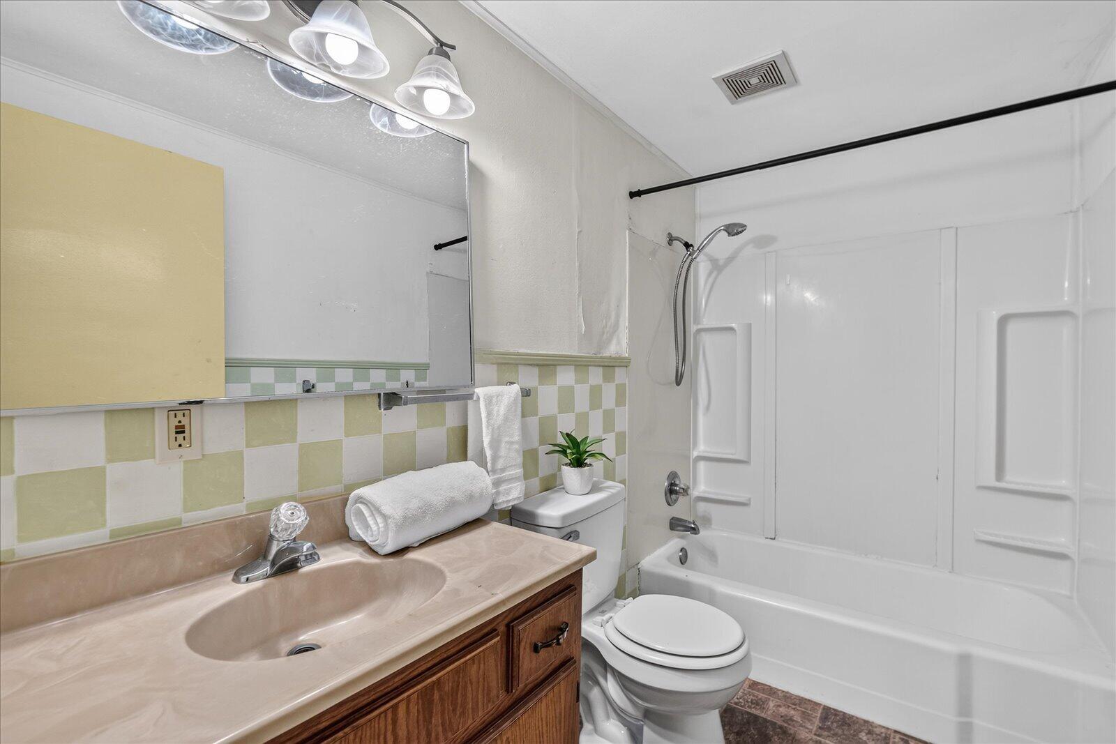Bathroom with beige vanity, checkerboard tile, and white tub-shower enclosure.