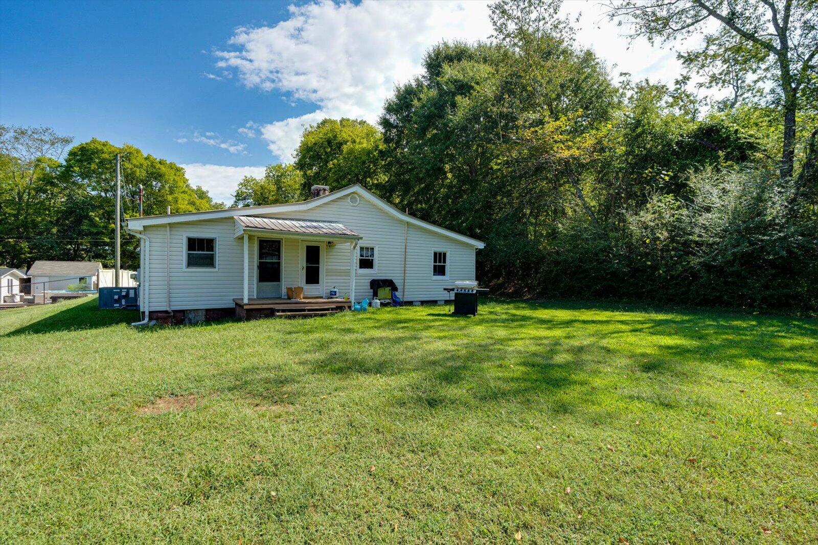 Single-story light-colored house with a small covered porch and broad grassy yard.