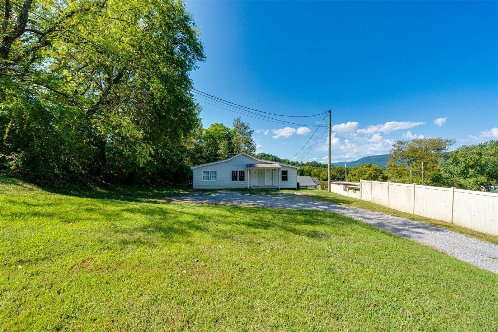 Small light-colored house at the end of a gravel driveway, with a broad lawn and distant mountain.