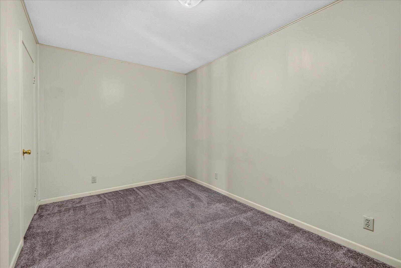 Empty carpeted room with light walls and a closed door.