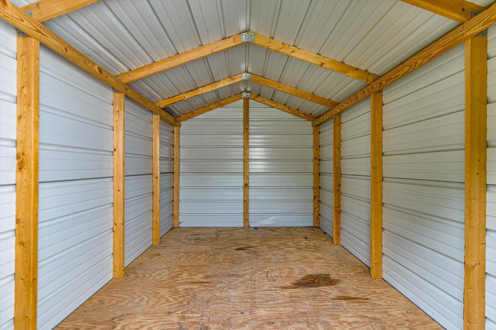 Empty storage shed with white metal walls, exposed wood framing, and a plywood floor.