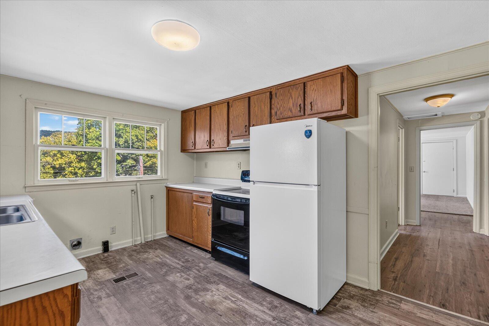 Kitchen with wood cabinets, white refrigerator, black range, and windows overlooking trees.