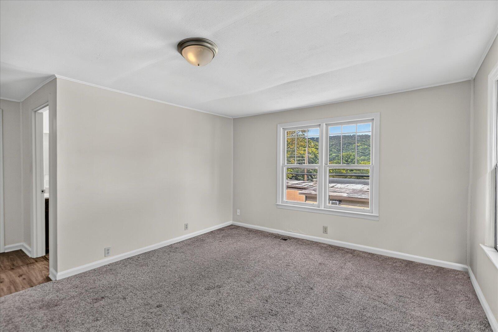 Empty bedroom with gray carpet and a window overlooking wooded hills.