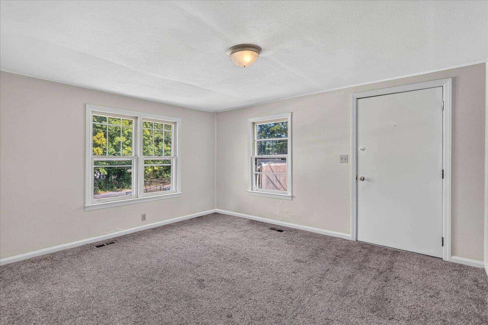 Empty carpeted room with neutral walls, three windows, and a white door.