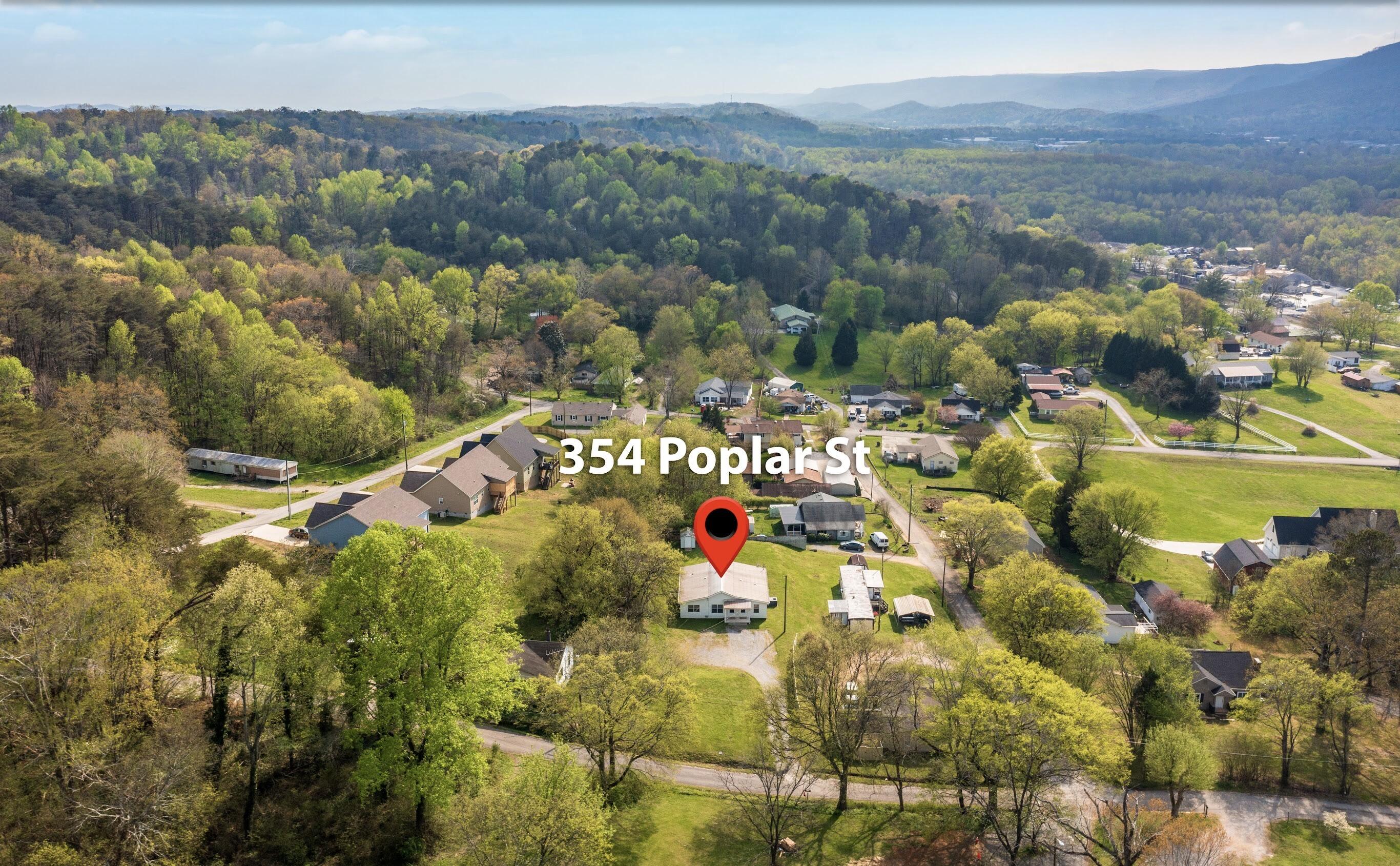 Aerial view of 354 Poplar Street in a wooded neighborhood, with distant mountain ridges.