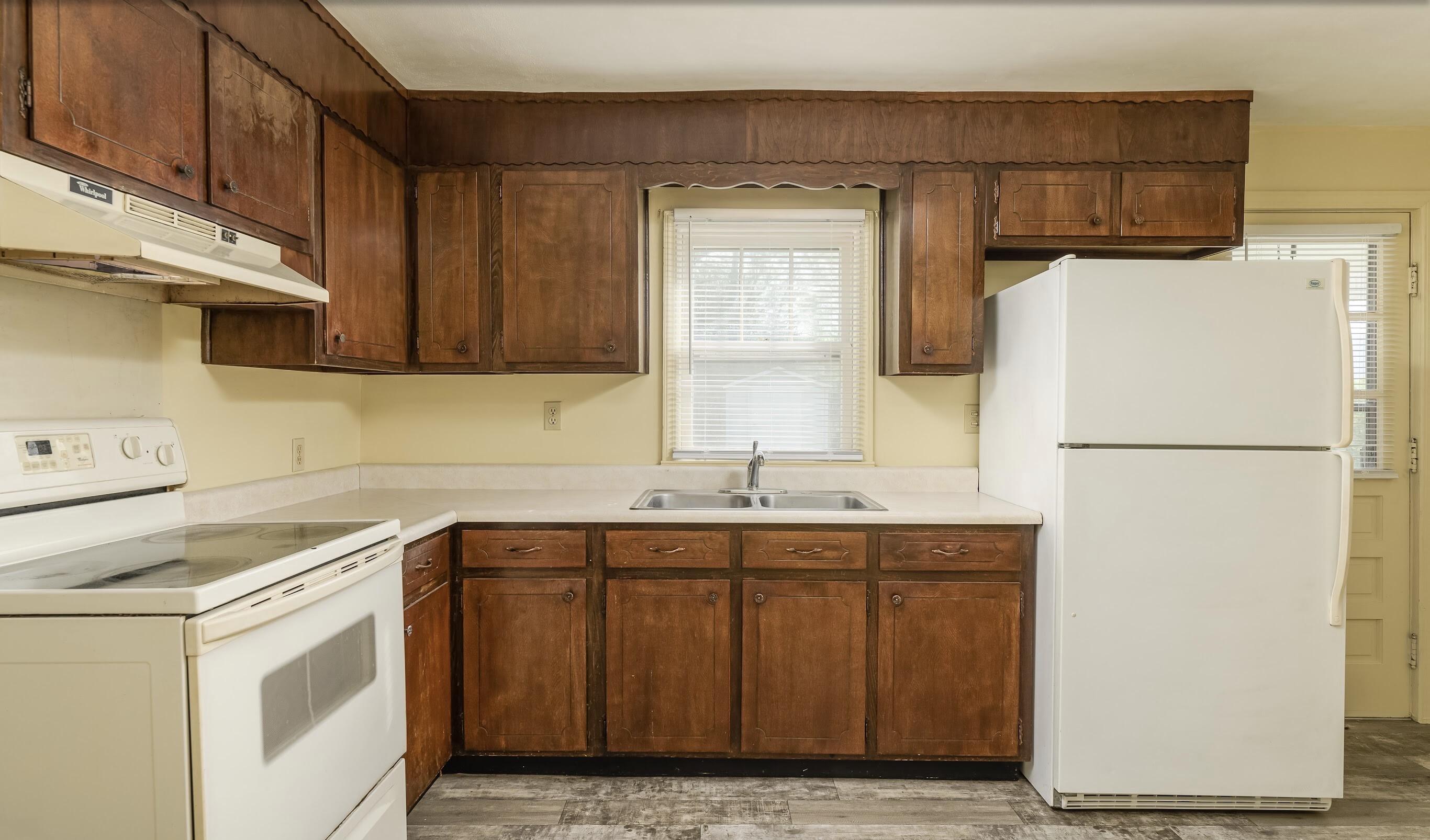 Kitchen with dark wood cabinets, white appliances, and a sink beneath a window.