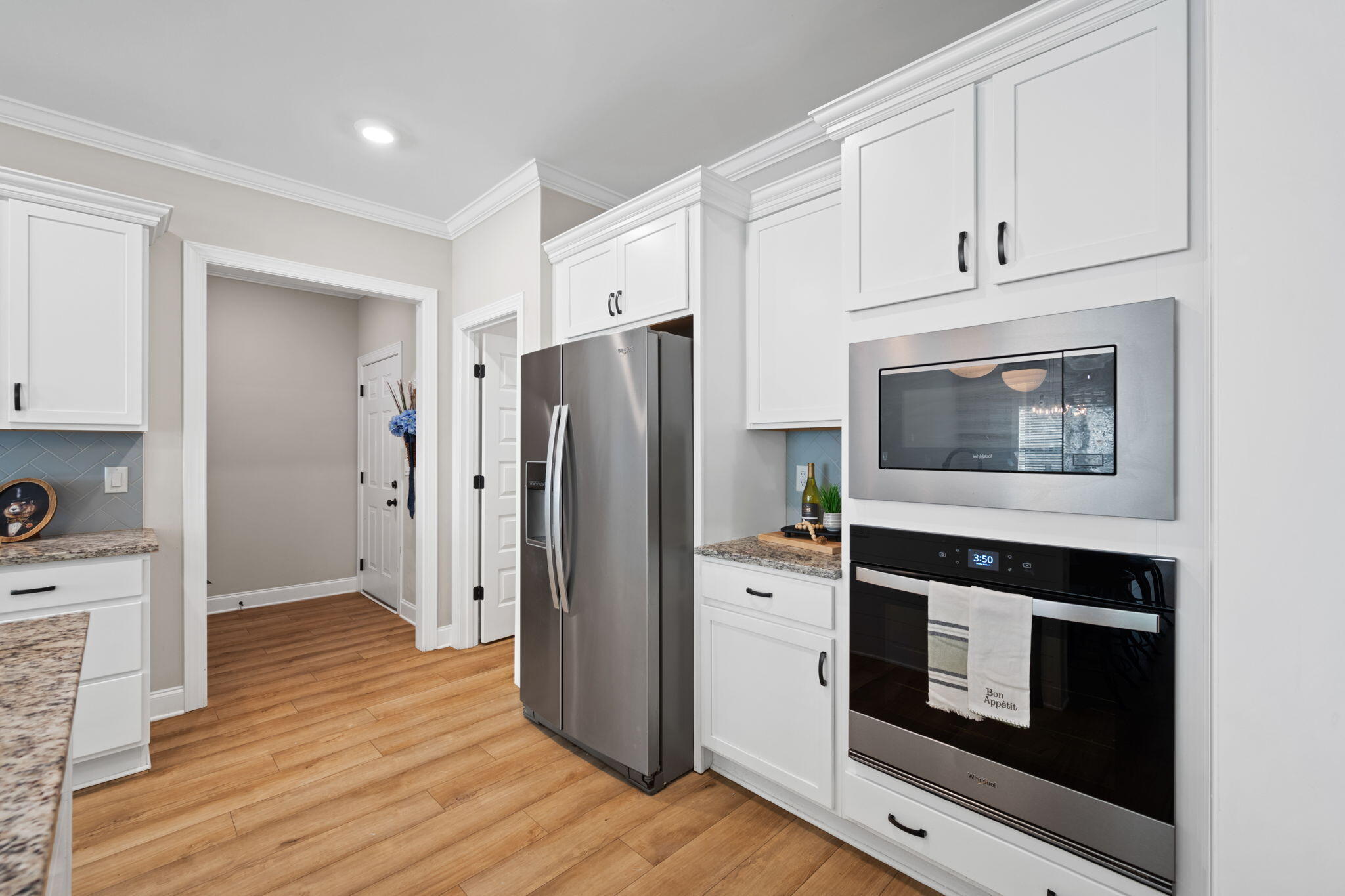 Kitchen with white cabinetry, granite counters, stainless-steel appliances, and warm wood flooring.