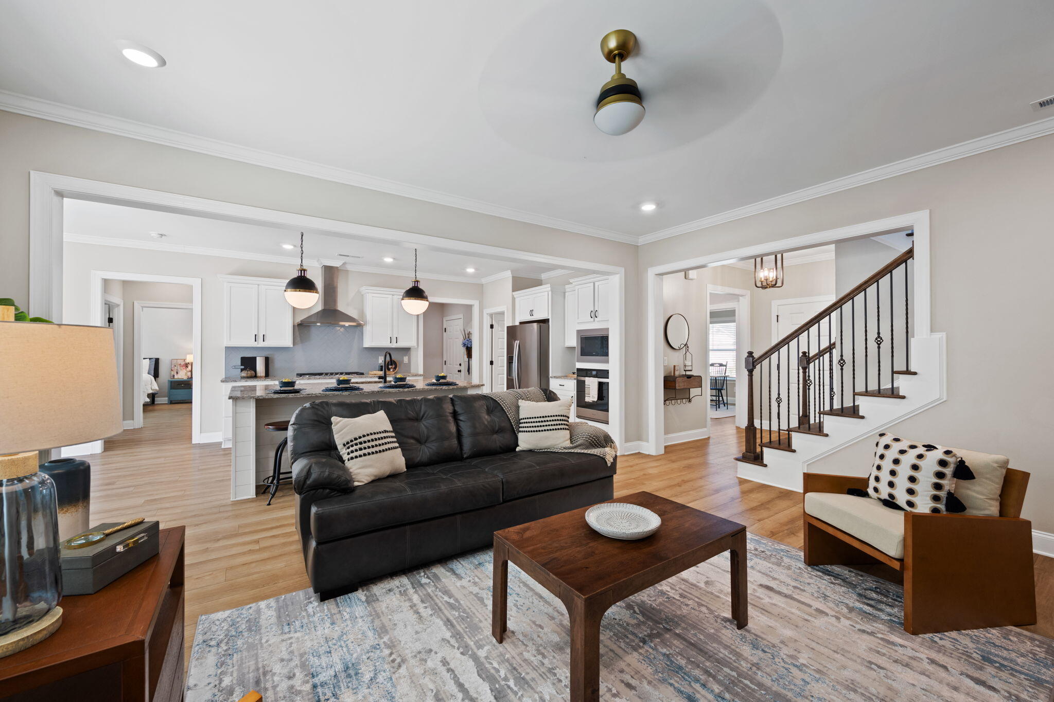 Open-plan living room with black leather sofa, white kitchen island and cabinetry, and staircase with iron balusters.