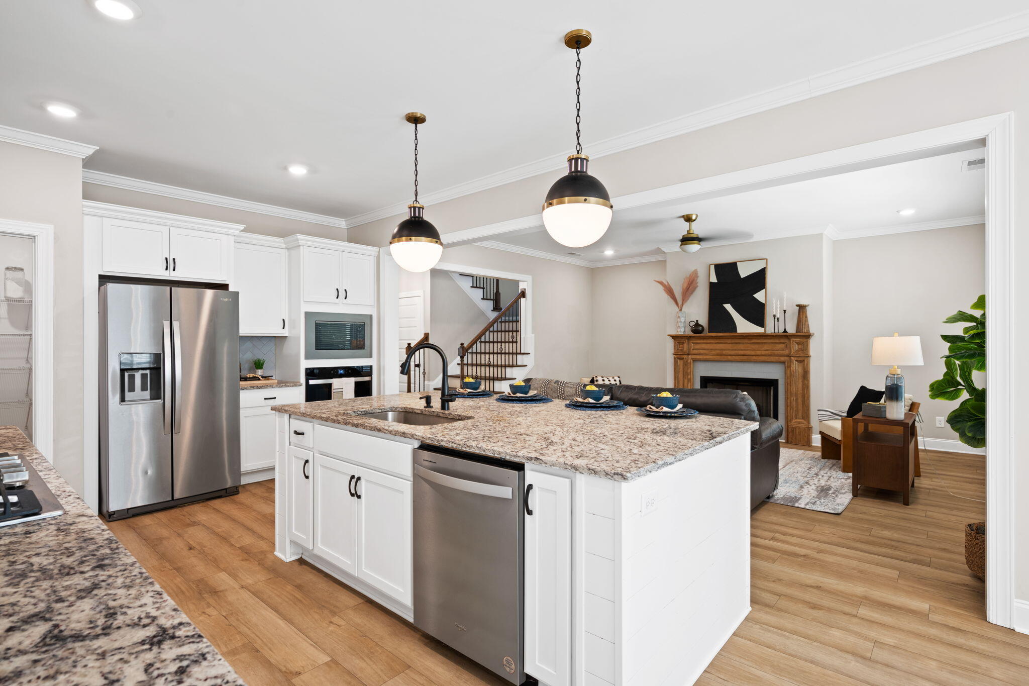 Open kitchen with a large granite island, white cabinets, stainless appliances, and a living room with fireplace.