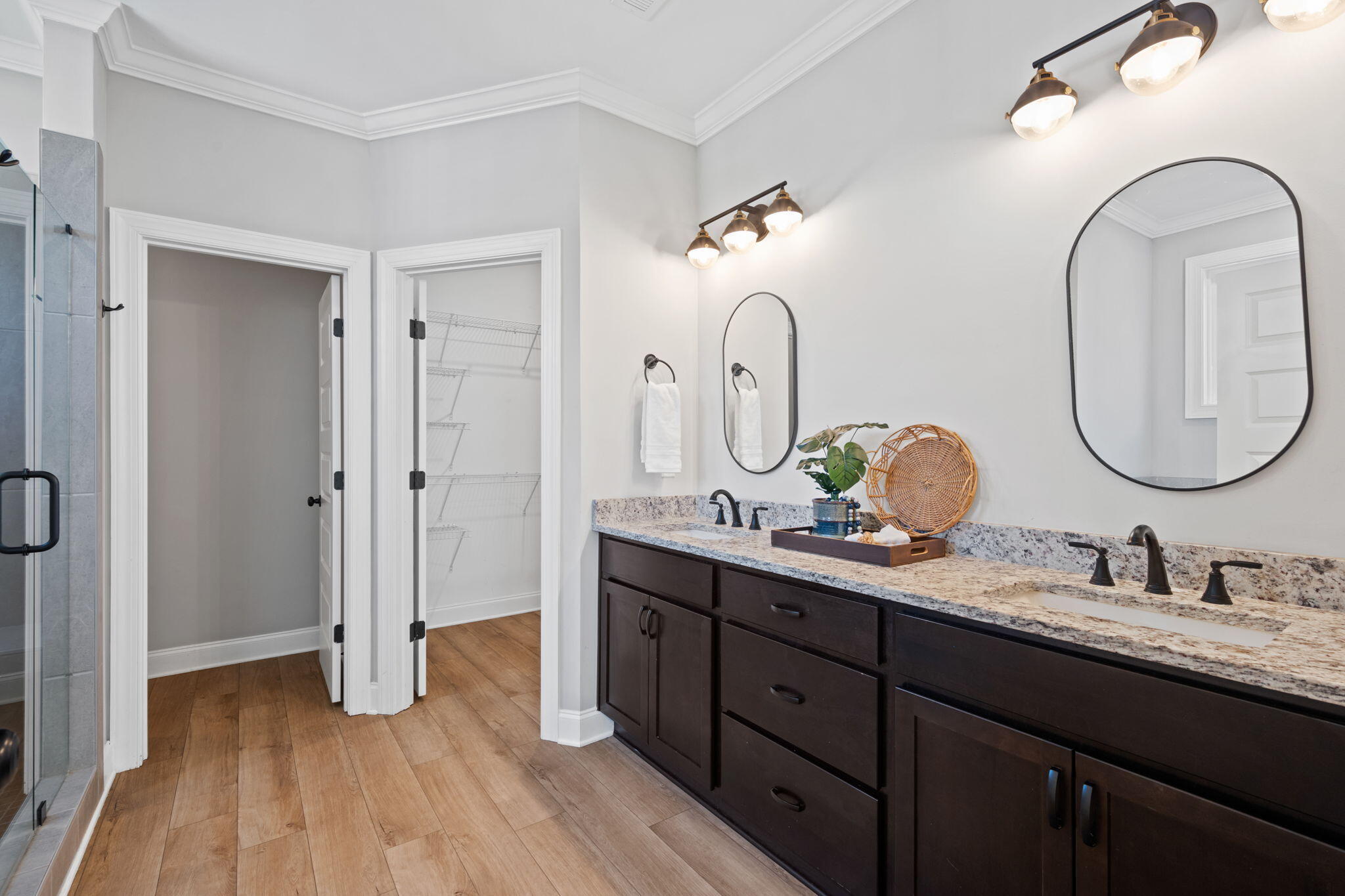 Bathroom with dark double vanity, two oval mirrors, glass shower, and an open walk-in closet.
