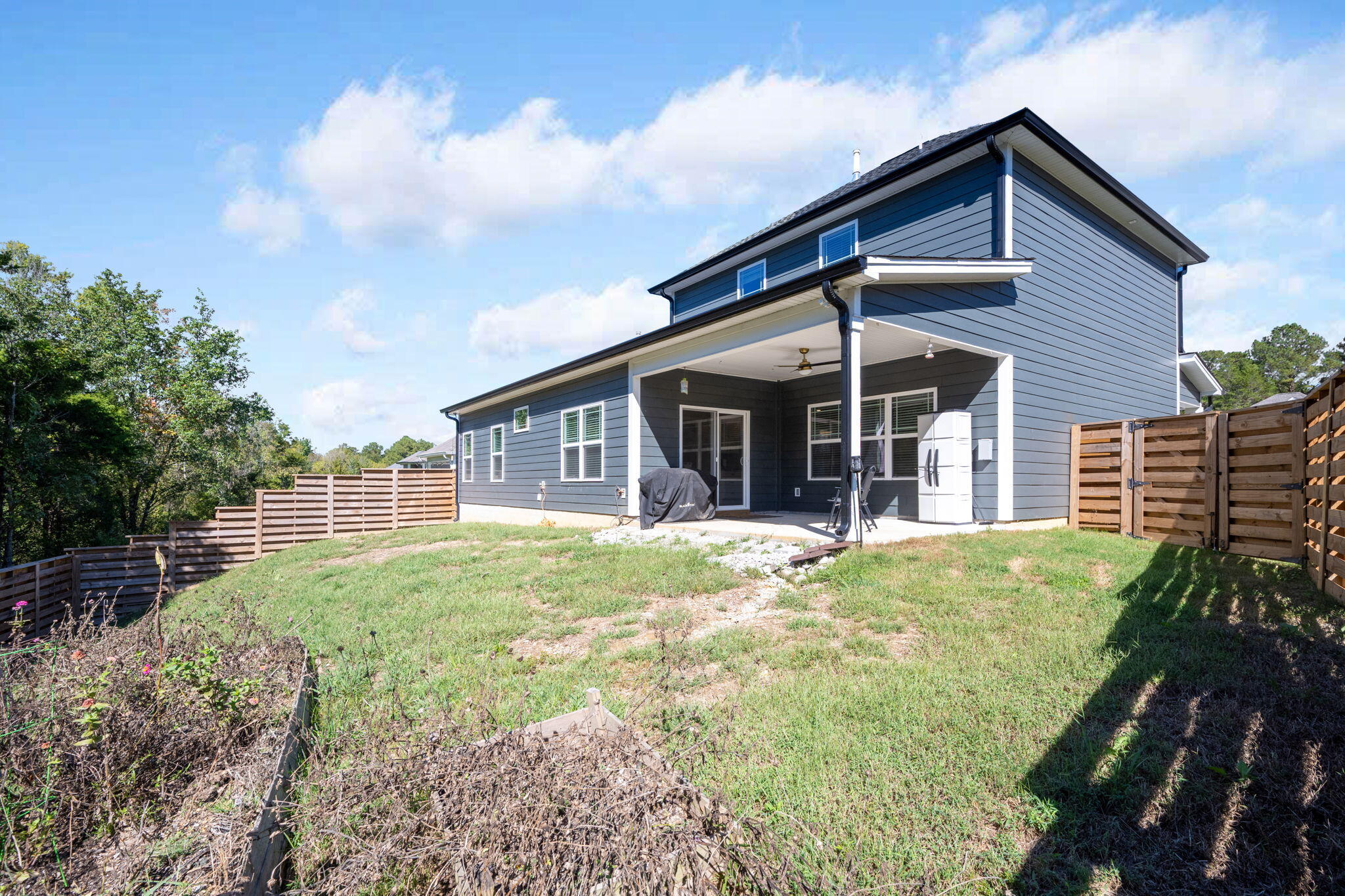 Two-story blue-sided home with a covered patio and fenced backyard.